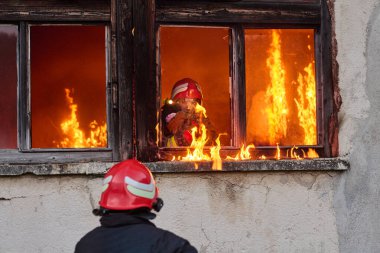 İtfaiyeciler yanan bir binada alevlerle savaşıyor. Bu görüntü itfaiyecilerin karşılaştığı tehlikeleri ve zorlukları ve acil durum müdahalesinin önemini göstermek için kullanılabilir.