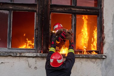 İtfaiyeciler yanan bir binada alevlerle savaşıyor. Bu görüntü itfaiyecilerin karşılaştığı tehlikeleri ve zorlukları ve acil durum müdahalesinin önemini göstermek için kullanılabilir.