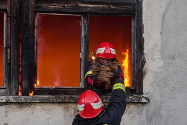 İtfaiyeciler yanan bir binada alevlerle savaşıyor. Bu görüntü itfaiyecilerin karşılaştığı tehlikeleri ve zorlukları ve acil durum müdahalesinin önemini göstermek için kullanılabilir.