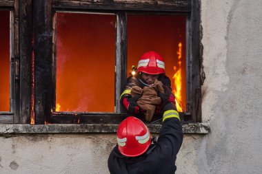 İtfaiyeciler yanan bir binada alevlerle savaşıyor. Bu görüntü itfaiyecilerin karşılaştığı tehlikeleri ve zorlukları ve acil durum müdahalesinin önemini göstermek için kullanılabilir.