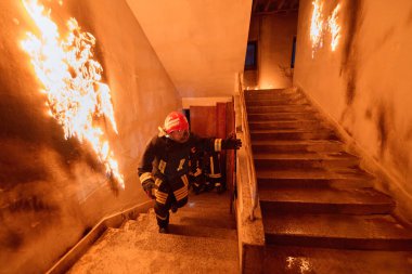 İtfaiyecilerden oluşan bir ekip, bir binanın içindeki merdivenlerde alevlerle savaşıyor. Görüntü, yangının önemini vurgulayarak acil müdahale durumlarının aciliyetini ve tehlikesini yakalıyor.