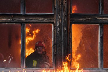 Yanan bir binanın penceresinden bir itfaiyeci görülüyor. Acil durum müdahalesinin tehlikesini ve yoğunluğunu gösteriyor. Bu görüntü yangın güvenliği, kurtarma operasyonları ve kahramanca çabaları vurguluyor.