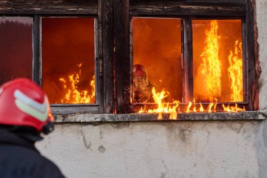 İtfaiyeciler yanan bir binada alevlerle savaşıyor. Bu görüntü itfaiyecilerin karşılaştığı tehlikeleri ve zorlukları ve acil durum müdahalesinin önemini göstermek için kullanılabilir.
