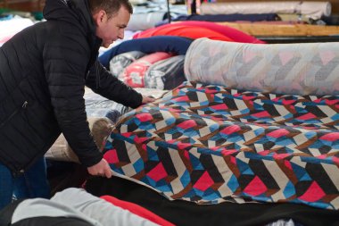 Tasarımcı bir tekstil deposunda renkli kumaş ruloları seçiyor. Dikiş dikmek için malzeme seçiyor. Görüntü tekstil endüstrisi, malzeme seçimi veya