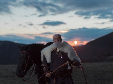 Büyük siyah bir at üzerindeki bir Viking savaşçısı gün batımında tüylü bir pelerin giyerek dramatik bir manzara keşfeder. Sahne, antik keşifleri, maceraları ve vahşi doğanın ruhunu çağrıştırıyor..