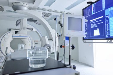 Bu modern tıbbi görüntüleme odasında teşhis için gelişmiş ekipmanlar var. Ekranlar hayati bilgiler ve görüntüler gösterirken, temiz bir kap laboratuvar masasında oturuyor.
