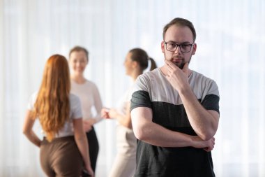 Gözlüklü ve gülümseyen genç bir adamın portresi. Gayri resmi bir iş görüşmesi sırasında arka planda meslektaşlarıyla dikilirken.