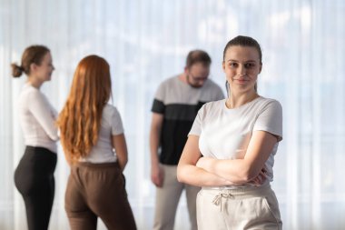 Kolları çapraz duran ve kameraya gülümseyen kendine güvenen bir kadının portresi.