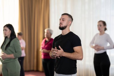 Bir grup kadın ve erkek, elleri karnında, içeride dikilip derin nefes egzersizleri yapıyorlar. Farkındalık, rahatlama ve sağlık eğitimi kavramı