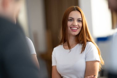 Gülümseyen ve kameraya bakan neşeli genç bir kadın. Kapalı alanda beyaz kıyafetlerle dikilirken. Pozitiflik, güven, mutluluk ve doğal güzellik kavramı