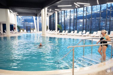 Modern bir kapalı kaplıca havuzunun kenarında oturan yaşlı bir kadın rahatlatıcı su jetlerinin keyfini çıkarıyor. Lüks bir kaplıcada ya da sağlık merkezinde rahatlık ve rahatlama kavramı