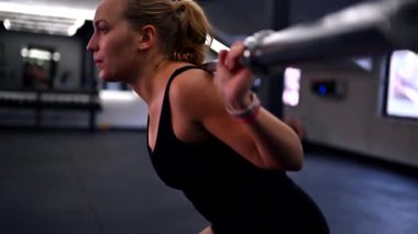Genç bir kadın spor salonunda ağırlık kaldırma egzersizleri yapıyor. Yoğun bir antrenman sırasında güç ve spor hedefleri üzerinde çalışırken kararlılık ve odaklanma gösteriyor..