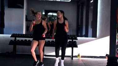 İki arkadaş spor salonunda egzersiz yapıyor, halterlerini kullanıyor ve antrenmanlarının tadını çıkarıyorlar. Aynı anda hem gülüşlerini, hem de motivasyonlarını paylaşıyorlar..