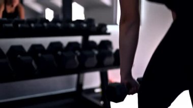 Bir fitness meraklısı, yoğun bir egzersiz sırasında güçlü ve kararlı bir şekilde, parlak bir spor salonunda dambıllarla sıkı antrenman yapar..