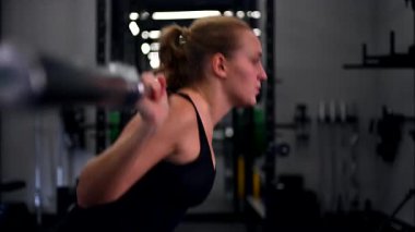 Kendini spora adamış bir sporcu spor salonunda ağırlık kaldırma antrenmanına başlar, halterle çömelirken doğru tekniğe konsantre olur. Çevre ciddi egzersizler için donatılmıştır..