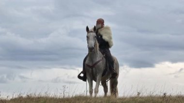 Hava aracı, kürk pelerinli Sakallı savaşçının beyaz bir ata binip gün doğumunda, arka planda dağları aştığını tespit ediyor. Tarihi, engebeli, maceralı bir sahne.