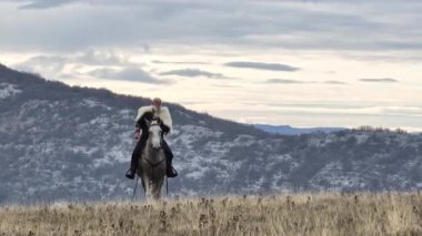 Hava aracı, kürk pelerinli Sakallı savaşçının beyaz bir ata binip gün doğumunda, arka planda dağları aştığını tespit ediyor. Tarihi, engebeli, maceralı bir sahne.