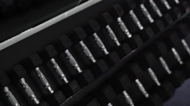 Modern bir spor salonundaki genç bir kadın idmanına başlamadan önce tertipli bir raftan dambıl alıyor. Temiz ekipmanlı şık fitness ortamı, güç eğitimi ve aktif yaşam tarzı