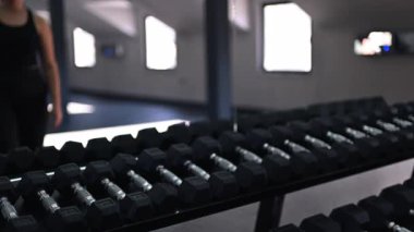 Bir insan spor salonunda dambıl seti kullanarak antrenman yapıyor. Parlak ve ferah ortam egzersiz deneyimini güçlendirir. Güç toplamaya odaklan..