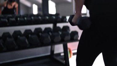 Kendini adamış bir birey, iyi aydınlatılmış bir spor salonunda çeşitli halter egzersizleri yapar. Motive edici bir ortamda ağırlık kaldırırken güç ve düzgün forma odaklanılır..