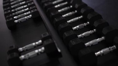 Modern spor salonundaki bir kadın yoğun bir idmandan sonra halterleri rafa kaldırıyor. Sahne düzgün bir jimnastik terbiyesi, organize ekipmanlar ve odaklanmış bir eğitim sonrası atmosferi gösteriyor..