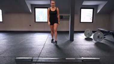 Spor salonunda bir atlet kaldırma için hazırlanıyor. Yer, siyah döşeme ve ekipmanlarla modern, odaklanmış bir çalışma ortamı sergiliyor..