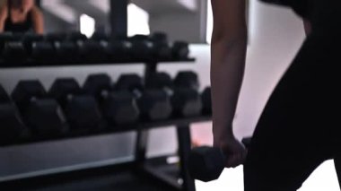 Bir fitness meraklısı, yoğun bir egzersiz sırasında güçlü ve kararlı bir şekilde, parlak bir spor salonunda dambıllarla sıkı antrenman yapar..