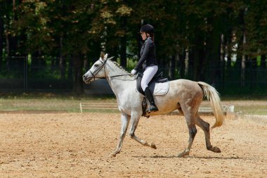 At biniciliği yarışında ata binen bir kadın binicilik sporlarındaki eğitim ve becerilerini sergiliyor. Bu resim atletizm, açık hava aktivitelerinin temaları ve