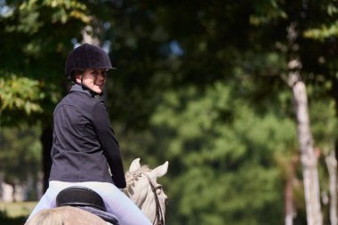 Gülümseyen bir kadın güneşli bir günde kırsalda at sürmekten hoşlanır. Bu görüntü binicilik sporları, açık hava aktiviteleri ve sağlıklı bir yaşam tarzı için mükemmel..