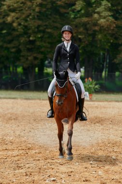 At biniciliği yarışında ata binen bir kadın binicilik sporlarındaki eğitim ve becerilerini sergiliyor. Bu resim atletizm, açık hava aktivitelerinin temaları ve