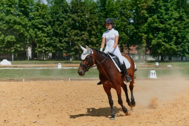 At biniciliği yarışında ata binen bir kadın binicilik sporlarındaki eğitim ve becerilerini sergiliyor. Bu resim atletizm, açık hava aktivitelerinin temaları ve