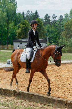 At biniciliği yarışında ata binen bir kadın binicilik sporlarındaki eğitim ve becerilerini sergiliyor. Bu resim atletizm, açık hava aktivitelerinin temaları ve