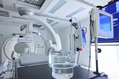Parlak bir tıbbi görüntüleme odasında teşhis için gelişmiş ekipmanlar bulunur. Cihazlar temiz bir ortamda hasta muayene ve tedavileri için hazırken, monitörler hayati bilgileri görüntüler.
