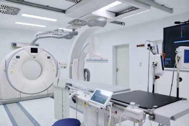 Gelişmiş tıbbi görüntüleme odasında, bir hastane ortamında teşhis için modern teknolojiyi sergileyen bir CT tarayıcı ve hasta muayene alanı bulunuyor..