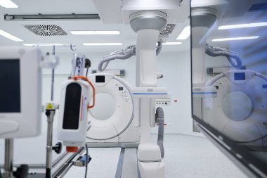 Temiz ve iyi aydınlatılmış bir hastane odasında gelişmiş tıbbi görüntüleme ekipmanları bulunuyor. Hasta muayeneleri sırasında kesin tanı konması için makineler kullanıma hazır..