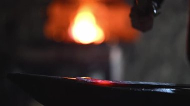 Beyaz sakallı ve örgülü saçları olan bir Viking demirci demircide çalışıyor. Örs üzerinde ışıldayan bir metal dövüyor. Arka planda alevler yanıp sönüyor.