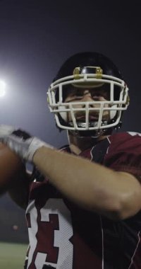 Amerikalı bir futbolcu sahada top atma ve yakalama pratiği yapıyor. Yüksek kalite sinematik yavaş çekim dikey görüntü