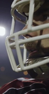 Tam teçhizatlı, siyah kask takmış ve kırmızı maske takmış, dramatik ışıklandırma ve yoğun odaklanma ile bir oyun anında yakalanan bir Amerikan futbolcusunun dikey yavaş çekimli sineması..