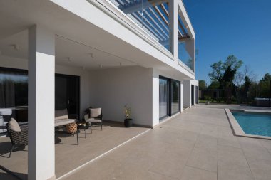 Güneşli bir günde havuzu, terası ve minimalist mimarisi olan modern lüks villa. Temiz hatlar, geniş pencereler ve açık yaşam alanları modern ev ortamları oluşturur..