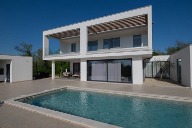 Güneşli bir günde havuzu, terası ve minimalist mimarisi olan modern lüks villa. Temiz hatlar, geniş pencereler ve açık yaşam alanları modern ev ortamları oluşturur..