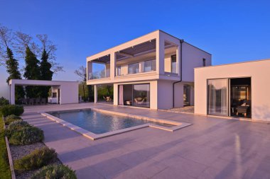 Güneşli bir günde havuzu, terası ve minimalist mimarisi olan modern lüks villa. Temiz hatlar, geniş pencereler ve açık yaşam alanları modern ev ortamları oluşturur..