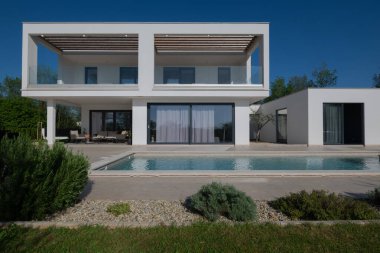 Güneşli bir günde havuzu, terası ve minimalist mimarisi olan modern lüks villa. Temiz hatlar, geniş pencereler ve açık yaşam alanları modern ev ortamları oluşturur..