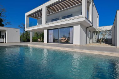Güneşli bir günde havuzu, terası ve minimalist mimarisi olan modern lüks villa. Temiz hatlar, geniş pencereler ve açık yaşam alanları modern ev ortamları oluşturur..