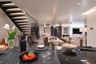 İçinde yüzen merdiven, mermer yemek masası, ahşap mutfak ve bej kanepe bulunan modern lüks iç mimari. Zarif ışıklandırması ve gri döşemeleri olan geniş çağdaş ev tasarımı..