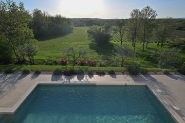 Açık mavi suyu olan modern bir yüzme havuzunun manzarası yükseldi. Parlak bir gökyüzü altında geniş yeşil alanlar, ağaçlar ve üzüm bağlarından oluşan bir manzaraya bakıyor. Huzurlu lüks için mükemmel.