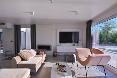 Günbatımında modern lüks oturma odası. Bej koltuklar, mermer yemek masası, parlak camlı büyük pencereler ve veranda manzaralı açık bir plan alanı. Çağdaş ev tasarımı.