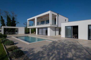 Güneşli bir günde havuzu, terası ve minimalist mimarisi olan modern lüks villa. Temiz hatlar, geniş pencereler ve açık yaşam alanları modern ev ortamları oluşturur..