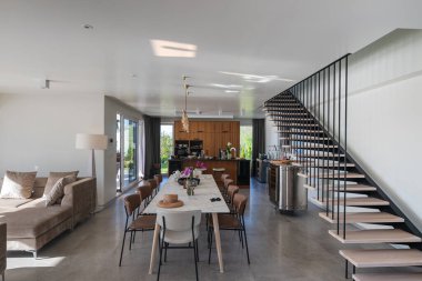 İçinde yüzen merdiven, mermer yemek masası, ahşap mutfak ve bej kanepe bulunan modern lüks iç mimari. Zarif ışıklandırması ve gri döşemeleri olan geniş çağdaş ev tasarımı..