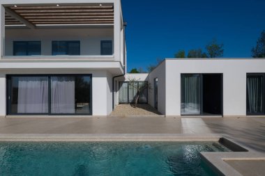 Güneşli bir günde havuzu, terası ve minimalist mimarisi olan modern lüks villa. Temiz hatlar, geniş pencereler ve açık yaşam alanları modern ev ortamları oluşturur..