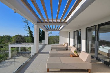 Güneş pansiyonlu modern lüks teras ve canlı yeşil manzaraya bakan ahşap pergola. Rahatlamak ve açık havada yaşamak için mükemmel. Gösterişli tasarım, cam korkuluklar ve doğal ışık..